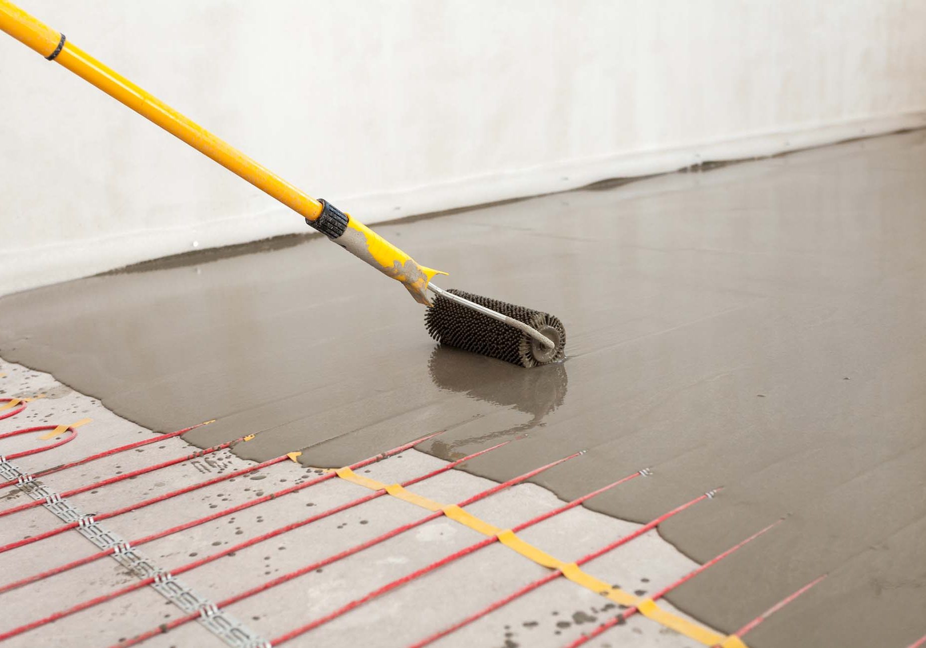 Electric floor heating system installation in new house. Worker align cement with roller